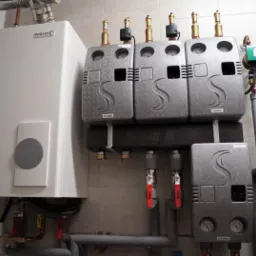 Biały piec gazowy z szarymi modułami COSMO i rurami w jasnym pomieszczeniu wyłożonym płytkami.