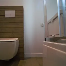 Nowoczesna toaleta podwieszana z drewnianą okładziną ścienną i przyciskiem spłukującym, widoczna r&oacute;wnież część kabiny prysznicowej.