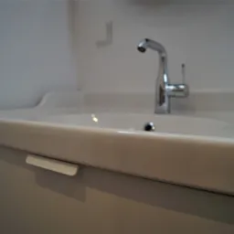 Nowoczesna biała umywalka z chromowaną baterią w minimalistycznej łazience, uchwyt szafki pod umywalką.