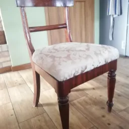 Krzesło w stylu retro z tapicerowanym siedziskiem w jasne wzory, widoczne drewniane nogi z ozdobnymi pierścieniami i oparcie w kolorze ciemnego drewna.