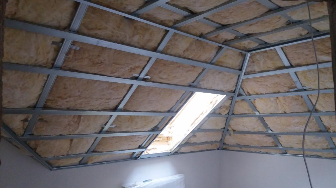 Poddasze w trakcie ocieplania wełną mineralną, widoczna metalowa konstrukcja pod płyty gipsowo-kartonowe oraz okno dachowe.