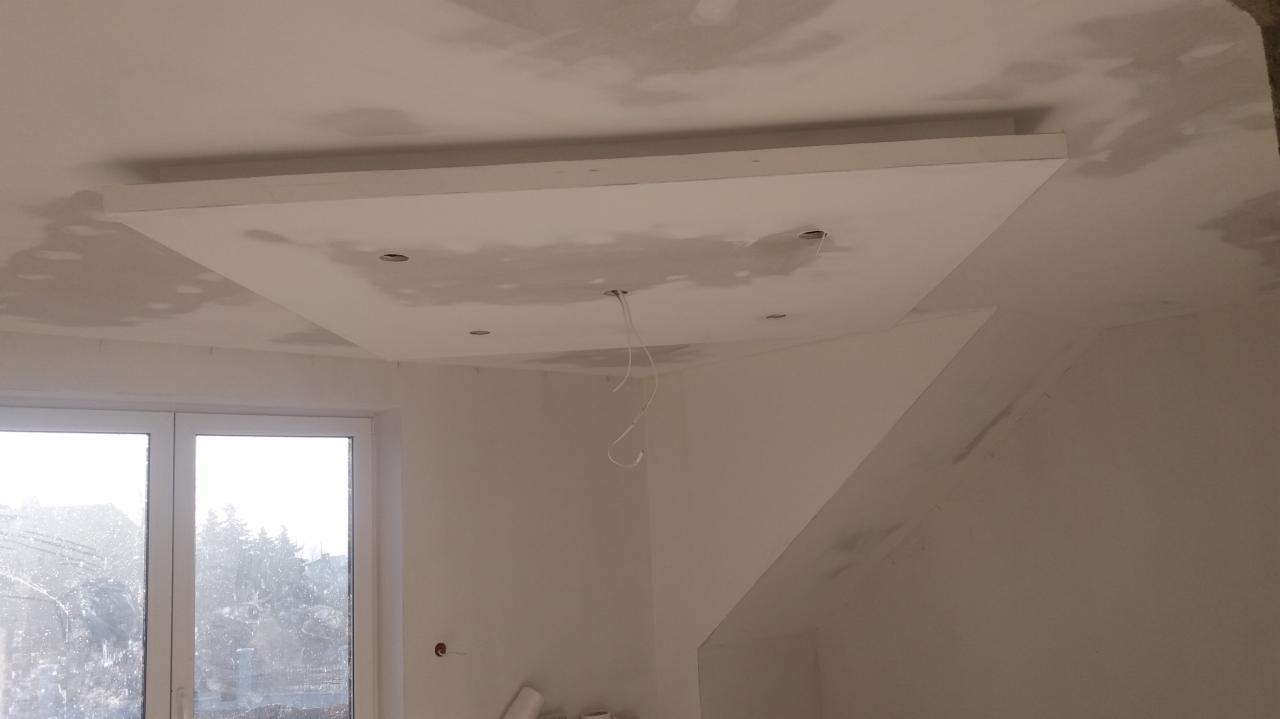 Sufit podwieszany z płyty gipsowo-kartonowej w trakcie szpachlowania, widoczne przewody oświetleniowe, okno w tle.