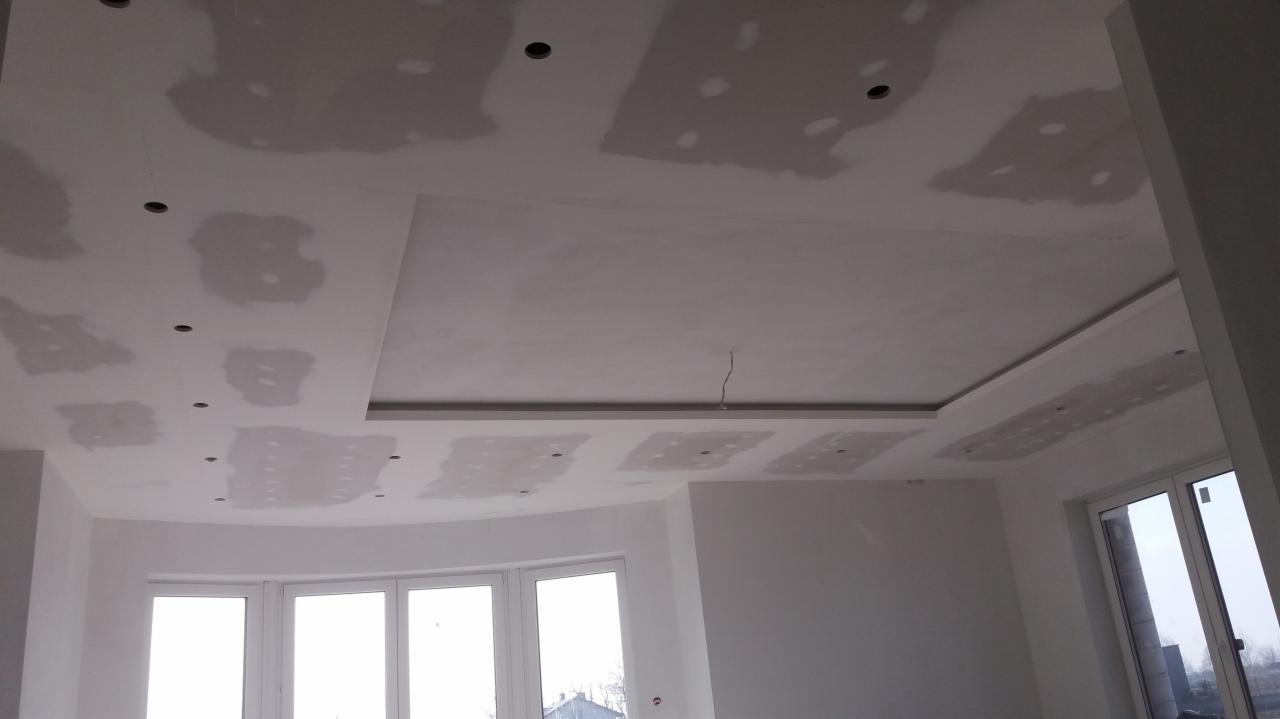 Niedokończony sufit z płyt kartonowo-gipsowych z widocznymi miejscami na oświetlenie punktowe i elementami dekoracyjnymi, przygotowany do dalszych prac wykończeniowych, takich jak szpachlowanie...