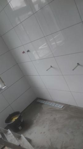 Wnętrze łazienki w trakcie kładzenia białych, błyszczących płytek ściennych, widoczny odpływ liniowy w posadzce i wiadro z zaprawą, przygotowane do fugowania.