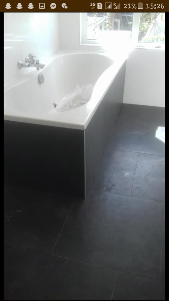 Biała wanna z chromowaną armaturą, obudowana ciemnoszarą płytą, na tle ciemnej podłogi z płytek w trakcie remontu łazienki, widoczne ślady po pracach.