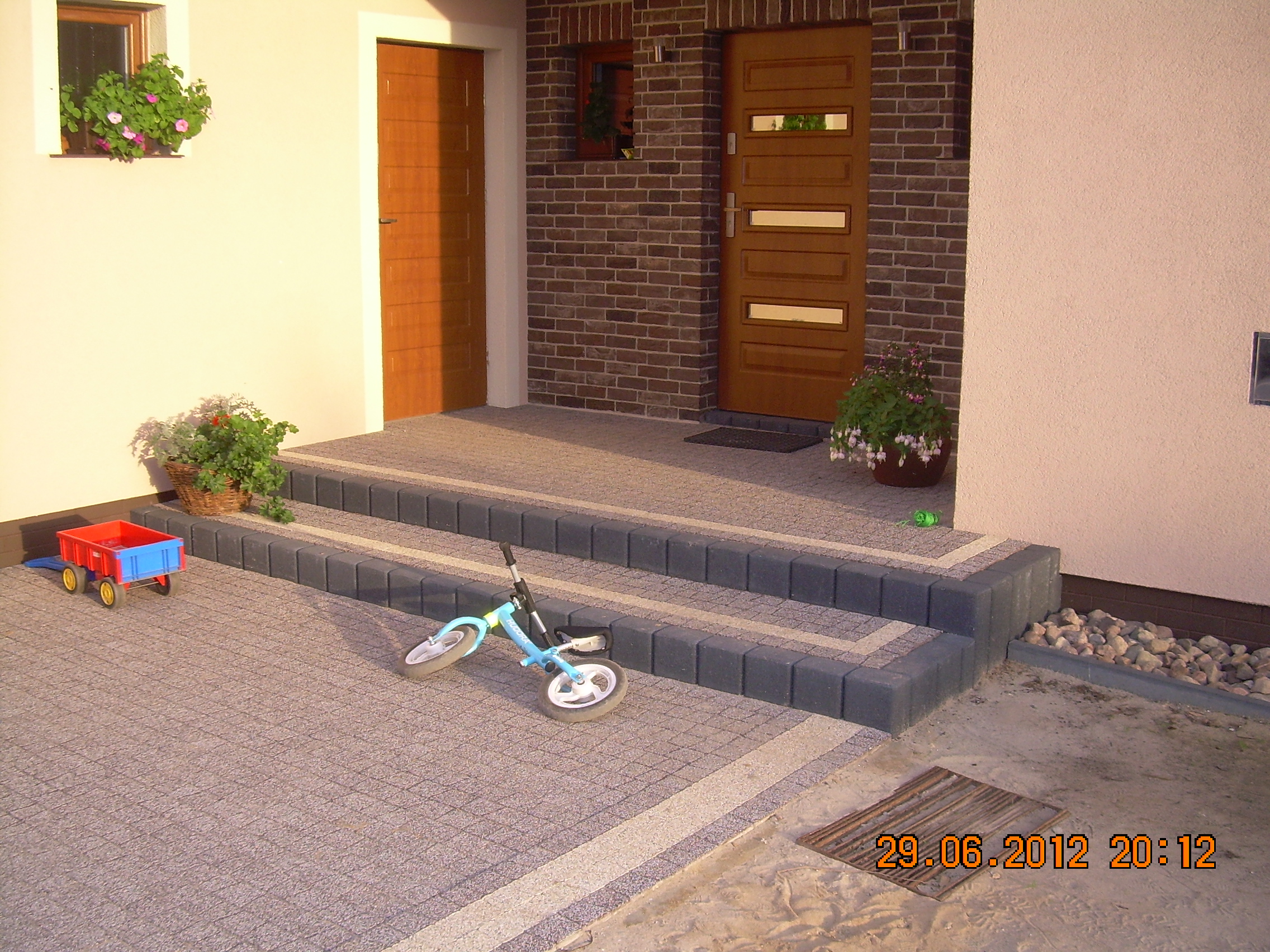 Ułożona kostka brukowa na podjeździe i schodach wejściowych do domu jednorodzinnego, zabawki dziecięce na kostce, widoczna data wykonania zdjęcia