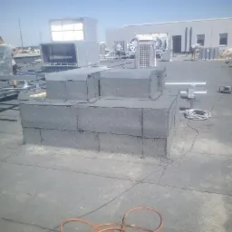 Montaż instalacji wentylacyjnej na płaskim dachu pokrytym papą, widoczne elementy wentylacyjne, uszczelnienia z papy, oraz przewody robocze.