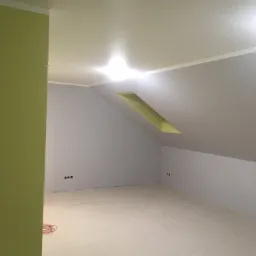 Pokój na poddaszu po remoncie, ściany częściowo pomalowane na szaro, częściowo na zielono, widoczne gniazdka elektryczne i kabel na podłodze.