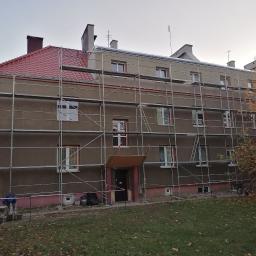 B.R.T. - Budynek wielorodzinny w trakcie prac elewacyjnych, z zamontowanym rusztowaniem, widoczne przygotowania do tynkowania i malowania elewacji, pracownicy w trakcie mieszania zaprawy. Częściowo...