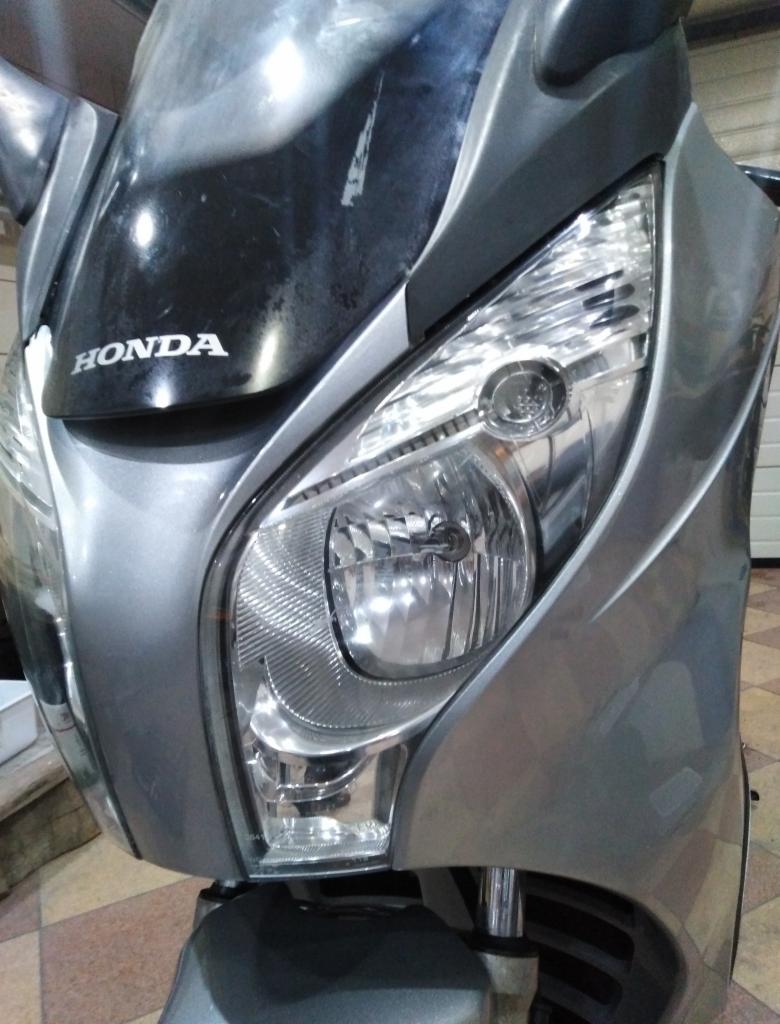 Przedni reflektor i owiewka motocykla Honda, widoczne ślady użytkowania na czarnej części owiewki.