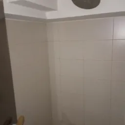 Wykończona kabina prysznicowa z beżowymi płytkami, okrągłą deszczownicą i odpływem liniowym w rogu.