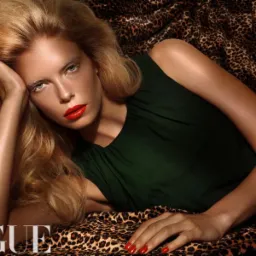 Portret kobiety w zielonej sukience leżącej na leopardziej tkaninie, z mocnym makijażem ust i paznokci w kolorze czerwieni, stylizowany na okładkę magazynu modowego.