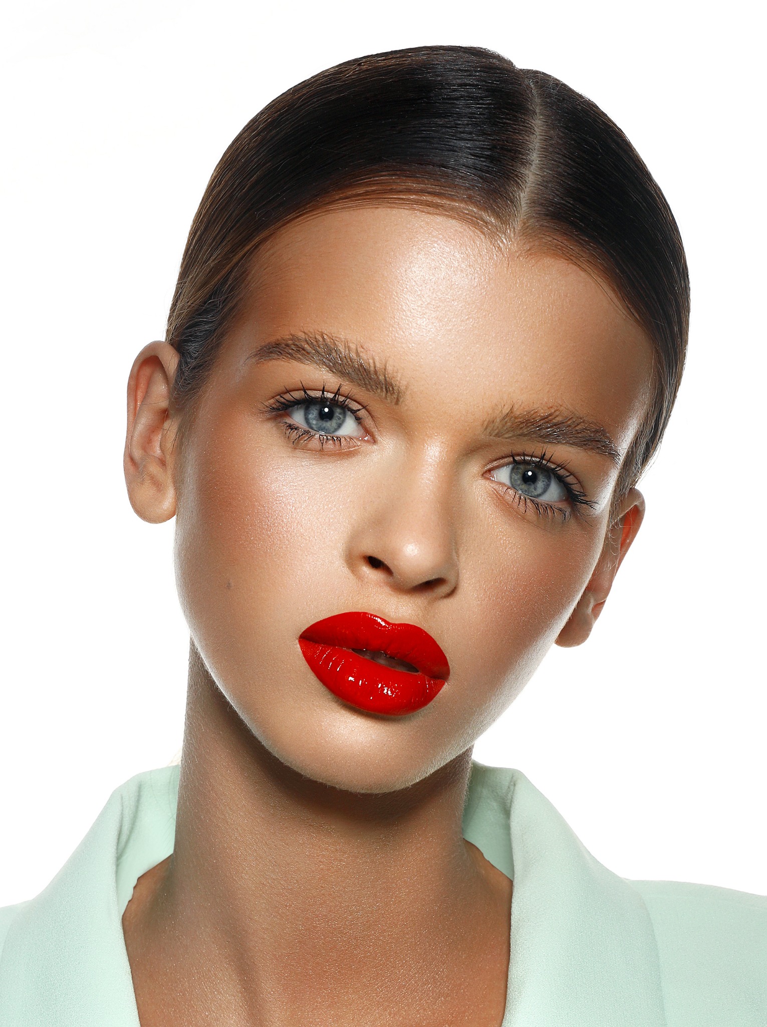 Portret modelki z intensywnie czerwonymi ustami i perfekcyjnie ułożonymi włosami, delikatny makijaż oczu, jasna skóra i pastelowa marynarka na białym tle.