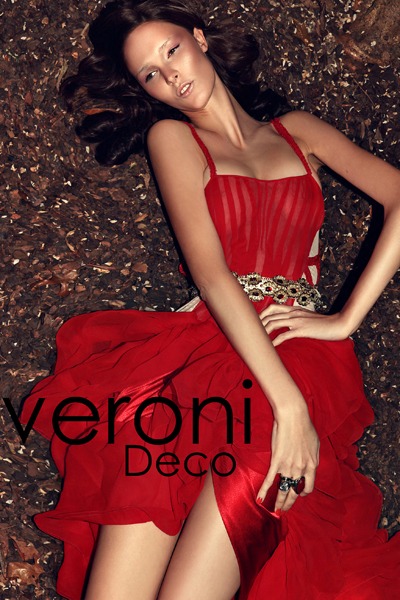 Kobieta leżąca na ściółce w czerwonej, zwiewnej sukni z ozdobnym paskiem, prezentacja marki Veroni Deco.