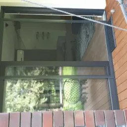 Zewnętrzna siatka przeciw owadom w oknie tarasowym, widok z drewnianego tarasu z wiszącym fotelem, ceglana podmurówka.