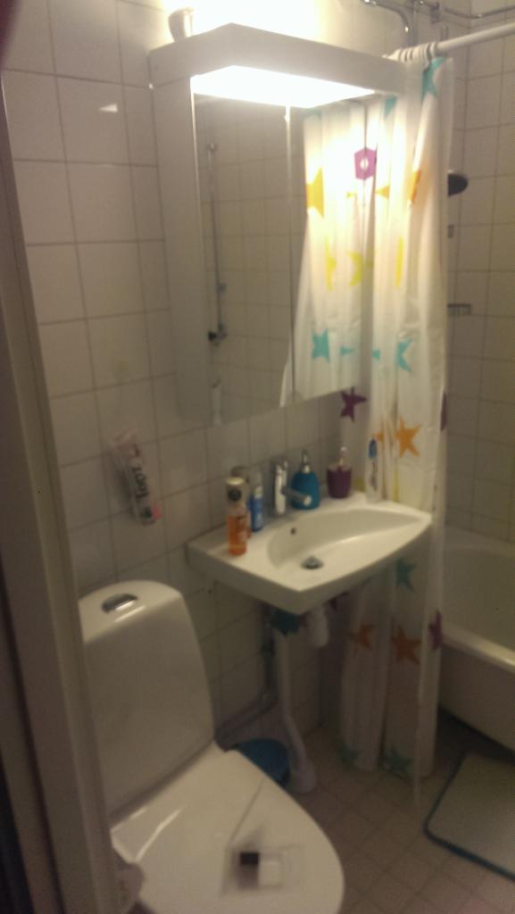 Łazienka z białą umywalką, toaletą i zasłoną prysznicową w gwiazdki, widok z perspektywy drzwi.