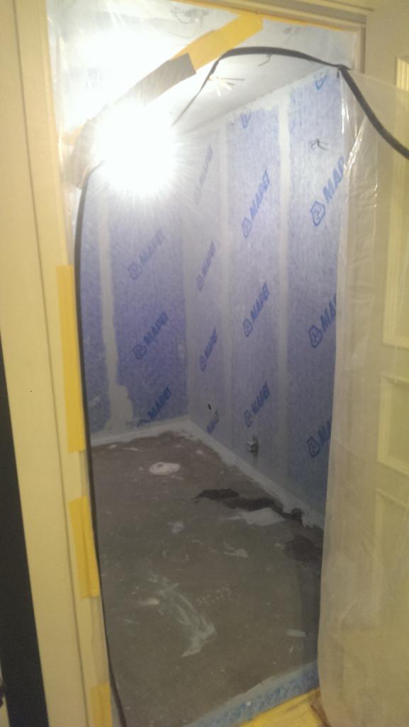 Wnętrze pomieszczenia zabezpieczone folią i taśmą malarską, ściany wyłożone niebieską membraną z nadrukiem MAPEI, przygotowane do dalszych prac wykończeniowych.