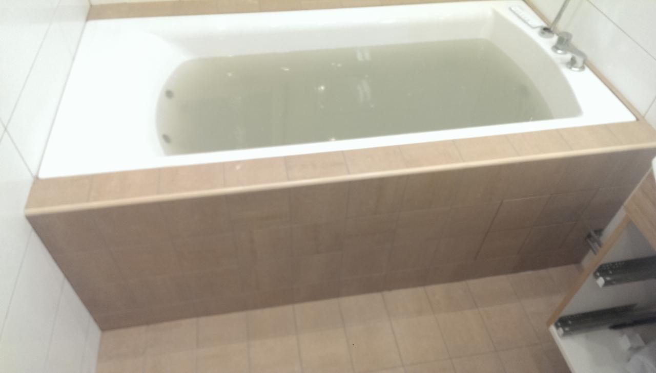 Wanna z brązową obudową z płytek, częściowo wypełniona wodą, widoczne białe płytki na ścianie i brązowe płytki na podłodze, ujęcie z góry.