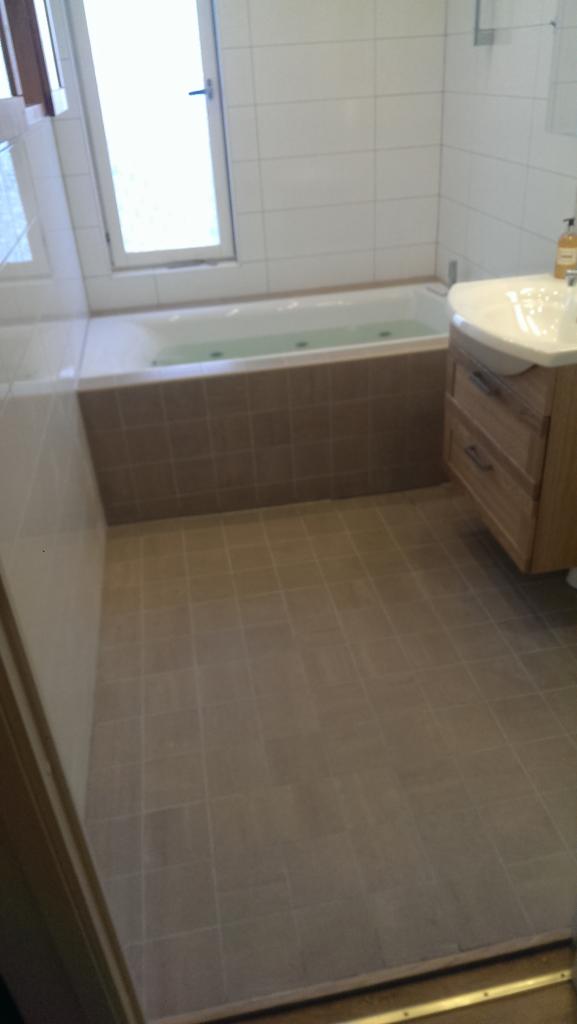 Ukończona łazienka z wanną z hydromasażem, umywalką z szafką z drewna i brązowymi płytkami na ścianach i podłodze.