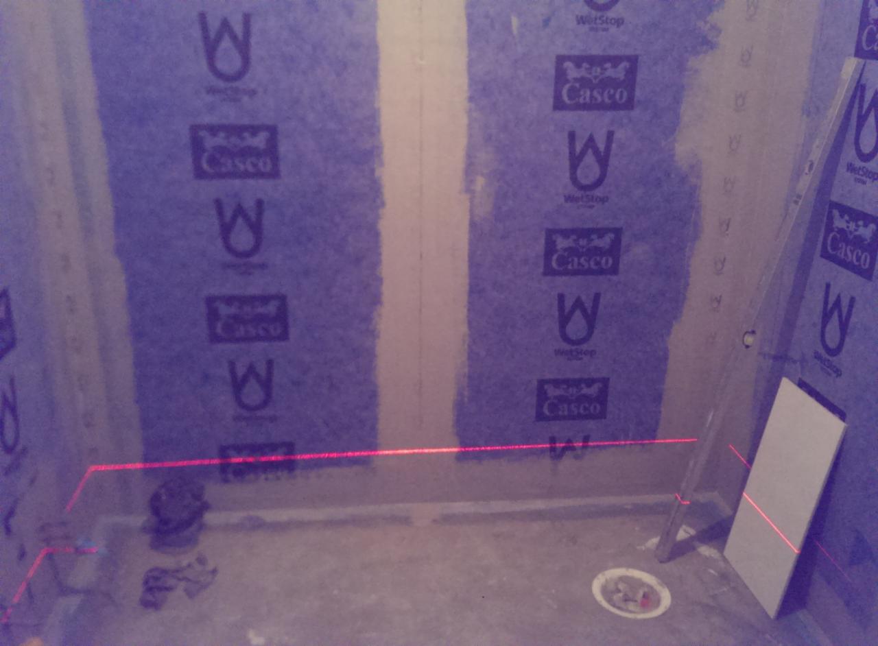 Montaż wodoodpornej płyty gipsowej Casco WetStop w narożniku łazienki, z użyciem poziomicy laserowej do precyzyjnego ustawienia.