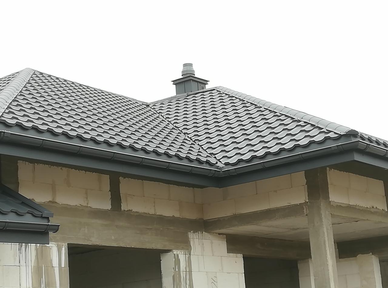 Szary dach z blachodachówki modułowej na surowym budynku w stanie deweloperskim, widoczne rynny i komin