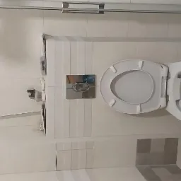 Wisząca toaleta z chromowanym przyciskiem spłukiwania na tle jasnych płytek w łazience po remoncie.