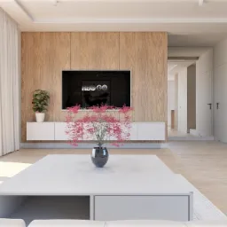 Jasne wnętrze salonu z drewnianą ścianą, telewizorem, białymi szafkami, roślinami w doniczkach i stolikiem kawowym z kwiatami, widziane z niskiej perspektywy.