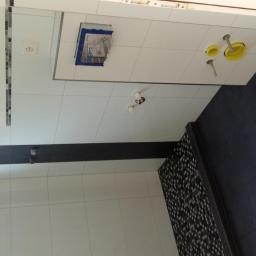 Lar-Bed - Wnętrze łazienki w trakcie remontu, widoczne białe płytki ścienne, fragment czarnej podłogi z płytek, instalacja sanitarna w ścianie oraz wystające przewody elektryczne.