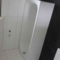 Lar-Bed - Wanna obudowana białymi płytkami, na ścianie widoczne przyłącza wodne, obok ciemne płytki imitujące kamień.