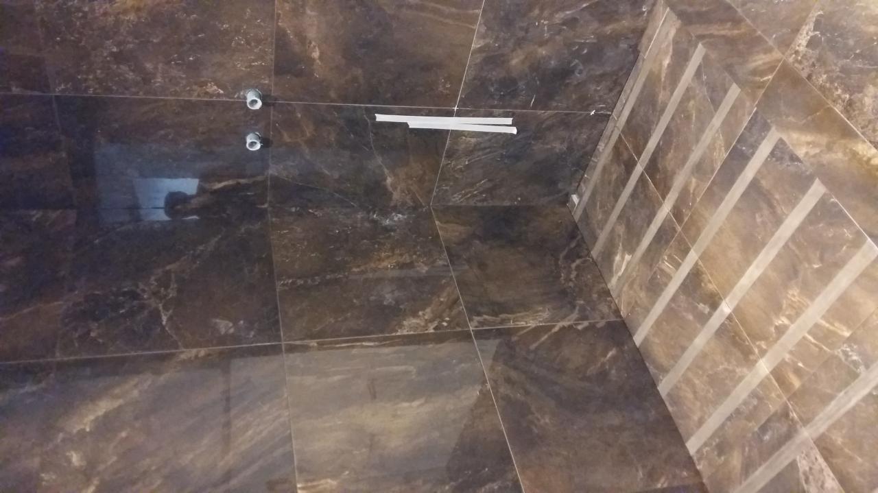 Ciemnobrązowe płytki imitujące marmur z jasnymi paskami dekoracyjnymi na ścianie w łazience w Wadowicach, widoczne przygotowane otwory na armaturę oraz białe paski taśmy malarskiej.