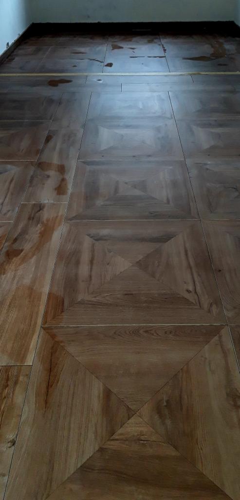 Ułożone panele podłogowe w geometryczny wzór z widocznymi łączeniami i odblaskami światła.