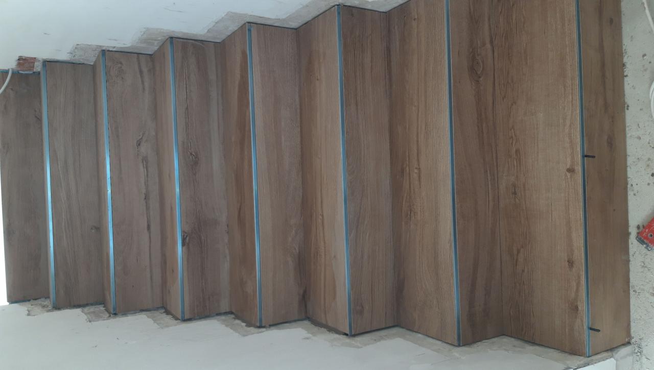 Wykończone schody z drewnopodobnymi panelami i metalowymi listwami, widoczne niedociągnięcia w wykończeniu sufitu i podłogi.