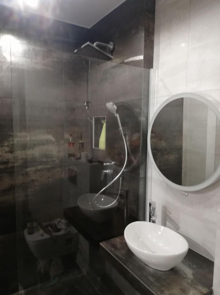 Nowoczesna kabina prysznicowa typu walk-in z deszczownicą i szklaną ścianką, dwie umywalki nablatowe oraz okrągłe lustro z podświetleniem w wykończonej łazience we Wrocławiu.