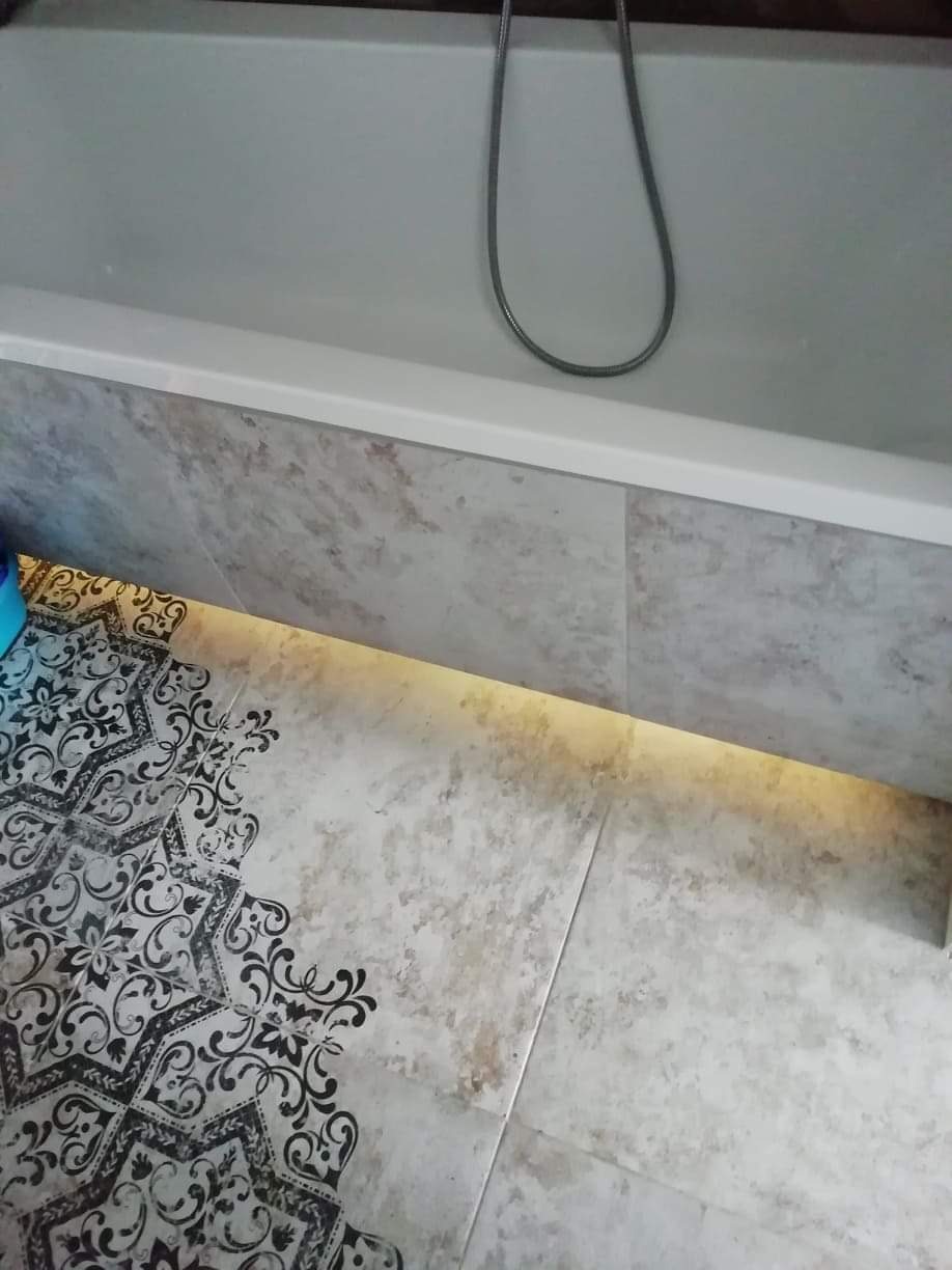 Fragment wykończonej łazienki z wanną, dekoracyjnymi płytkami podłogowymi w czarno-białe wzory oraz podświetleniem LED pod wanną.