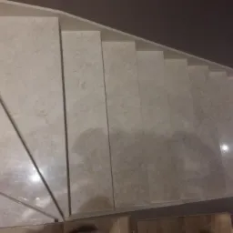 Widok z góry na wykończone schody z jasnych, marmurkowych płytek ceramicznych, z widocznym fragmentem podłogi na dole kadru.