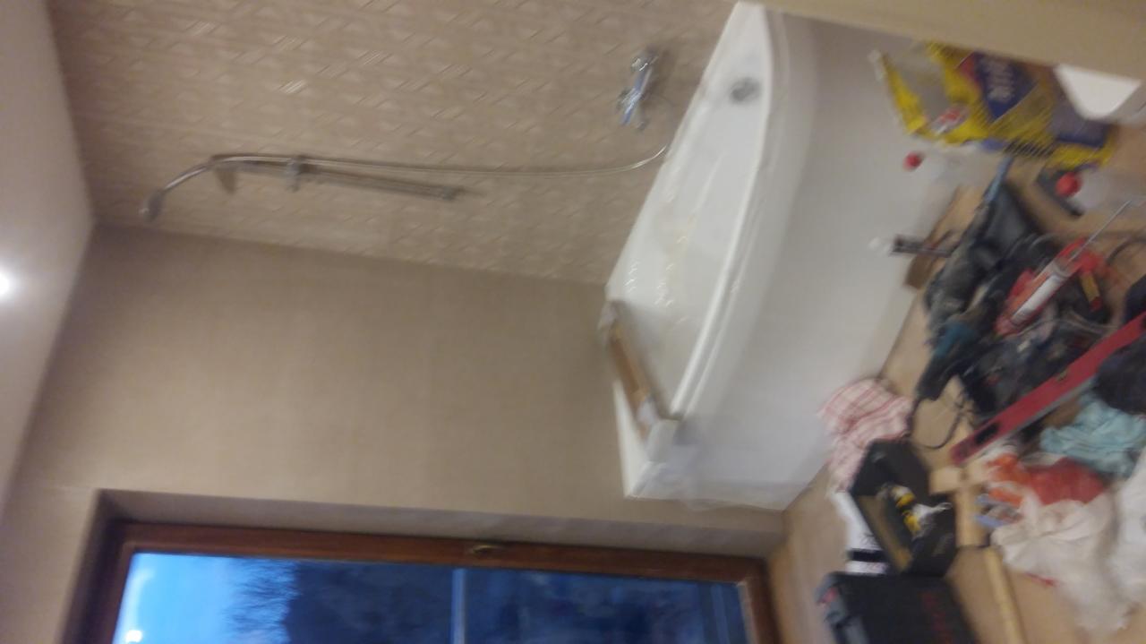 Wanna w folii ochronnej podczas remontu łazienki, widoczne narzędzia i materiały budowlane na podłodze, sufit z wzorem i instalacja prysznicowa.