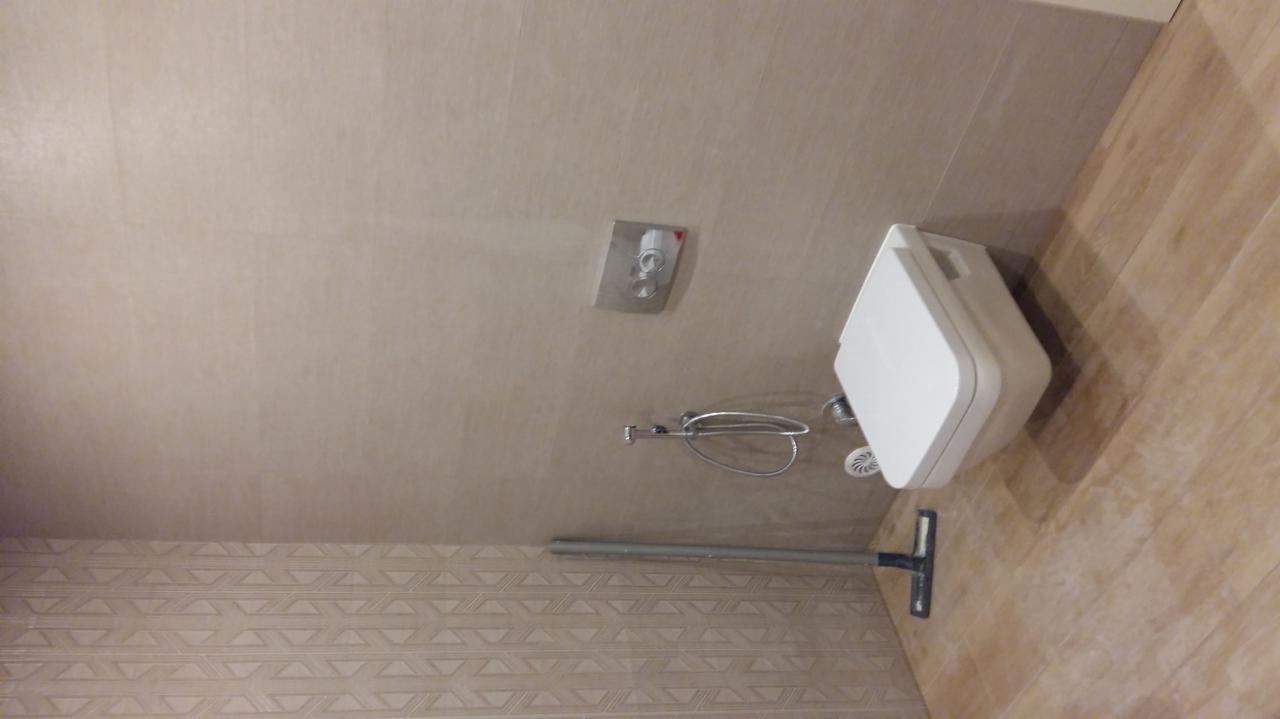 Nowoczesna toaleta podwieszana z chromowanym przyciskiem spłukiwania na ścianie, widoczny wąż natryskowy i delikatny wzór na dolnej części ściany.