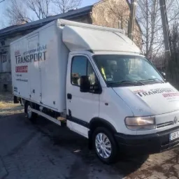 Biały samochód dostawczy z zabudową kontenerową i napisem 'bielski transport' na tle budynku.