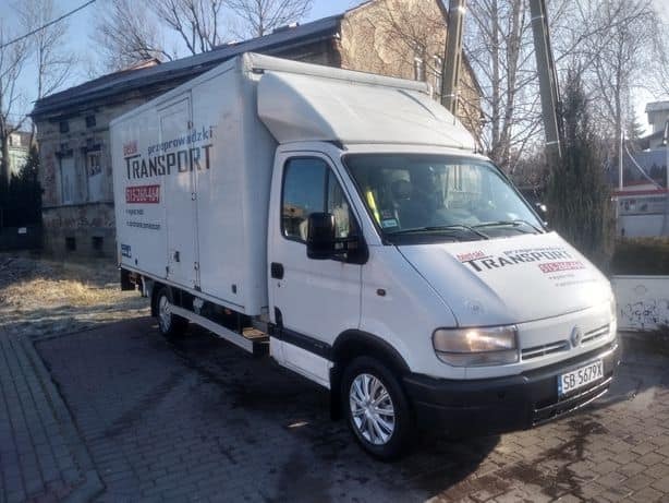 Biały samochód dostawczy z zabudową kontenerową i napisem 'bielski transport' na tle budynku.