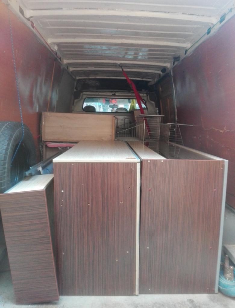 Wnętrze furgonetki wypełnionej meblami z ciemnego drewna, widoczna opona i elementy mocujące ładunek.