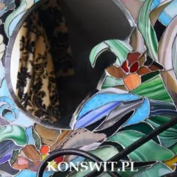 Stylowe lustro w ramie ze szkła witrażowego z motywem kwiatowym i ptasim, odbijające zasłony w tle.