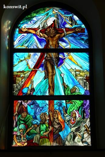 Witraż przedstawiający ukrzyżowanie Jezusa Chrystusa, z postaciami w dole spoglądającymi w górę, wykonany w żywych kolorach i podzielony na trzy panele.