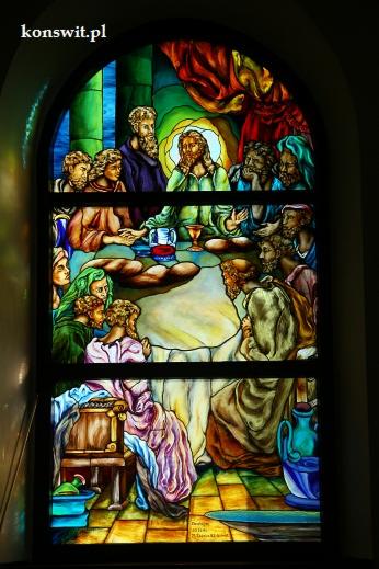 Barwne witraże przedstawiające Ostatnią Wieczerzę, umieszczone w łukowatym oknie kościelnym, z widocznymi detalami postaci i naczyń, oświetlone światłem dziennym.