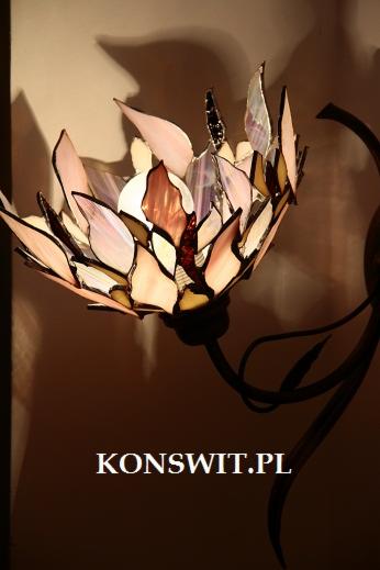 Lampa witrażowa w kształcie kwiatu lotosu, z elementami w odcieniach różu, fioletu i beżu, zamontowana na metalowym, stylizowanym ramieniu, oświetlona od wewnątrz, z widocznym adresem strony...