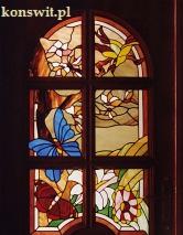 Stylowy witraż w drewnianej ramie okiennej przedstawiający motywy kwiatowe i motyla w żywych kolorach.