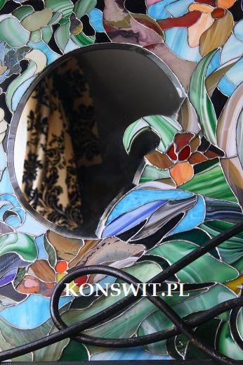 Stylowe lustro w ramie ze szkła witrażowego z motywem kwiatowym i ptasim, odbijające zasłony w tle.