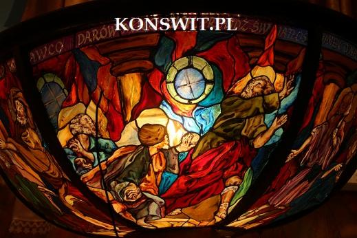 Kolorowy witraż przedstawiający scenę religijną z postaciami i okrągłym oknem, z widocznym adresem strony internetowej w górnej części.