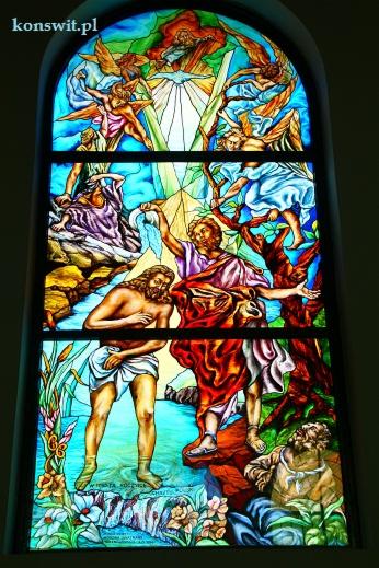 Barwne okno witrażowe przedstawiające scenę religijną z postaciami aniołów i ludzi w szatach, z wyraźnymi podziałami na panele i intensywnymi kolorami.