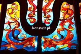 Fragment witrażu z motywem roślinnym w odcieniach czerwieni, pomarańczy, żółci i błękitu, widoczne detale spoin ołowianych.