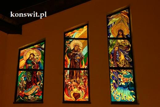 Trzy witraże w kościele przedstawiające postacie religijne, oświetlone od wewnątrz, z widocznym adresem strony internetowej w lewym górnym rogu.